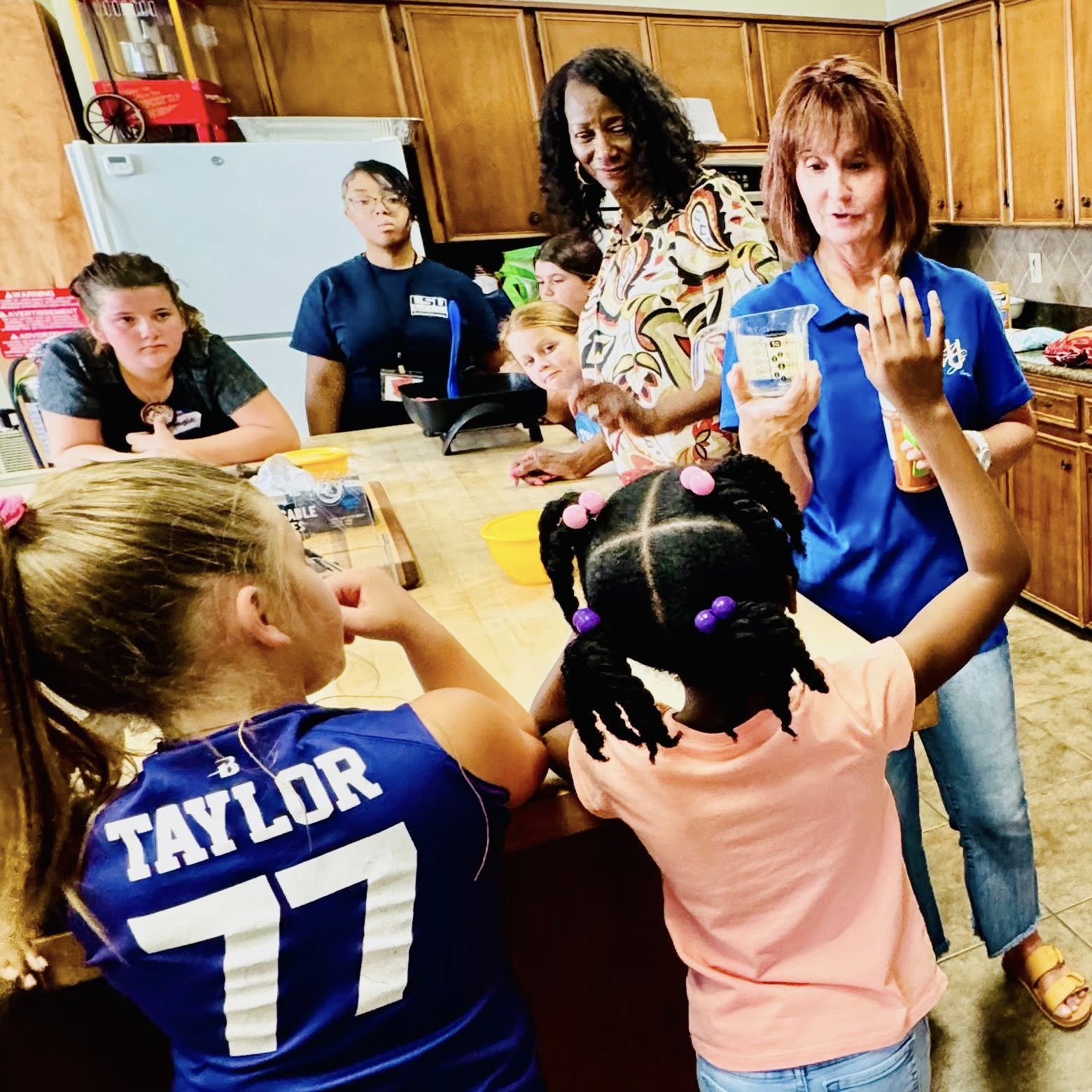 Two women and a group of girls standing around a counter.